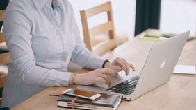 Person tippt auf einem Laptop, während sie an einem Tisch sitzt.