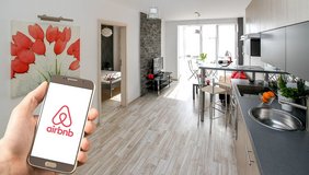 Person hält ein Smartphone und betrachtet ein modernes Wohnzimmer.