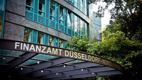 Fassade des Finanzamts Düsseldorf mit Bäumen im Vordergrund.