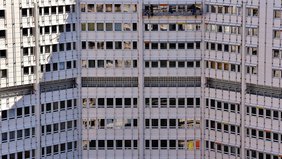 Fassade eines modernen Hochhauses mit zahlreichen Fenstern und Bauarbeiten oben.