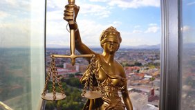 Statue der Justitia mit Waage und Schwert, mit Blick auf eine Stadtlandschaft.