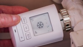 Elektronisches Heizungsthermostat mit Display und Bedienknopf in Hand gehalten.